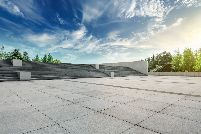 Large paved concrete plaza with wide stepped seating and surrounding trees