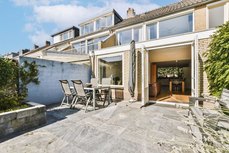 Paved outdoor patio area with seating beside a townhouse