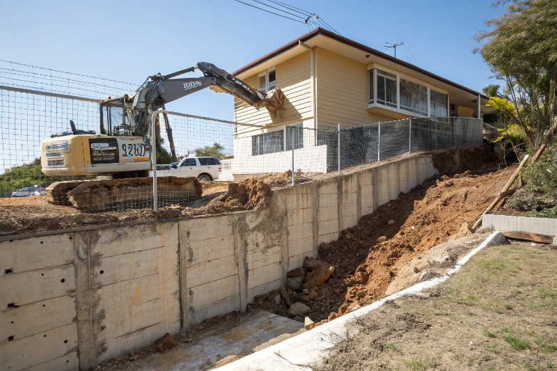 Excavator with hydraulic breaker demolishing concrete retaining wall on Ipswich residential property