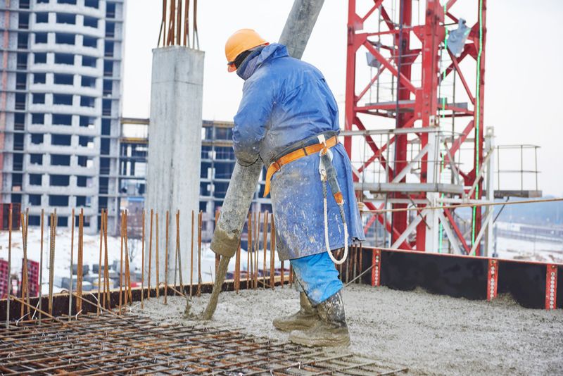Worker pouring concrete into rebar formwork at a high-rise construction site