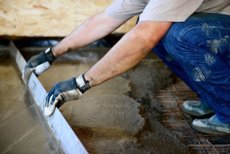 Tradesperson screeding wet concrete with an edging trowel over reinforcement mesh