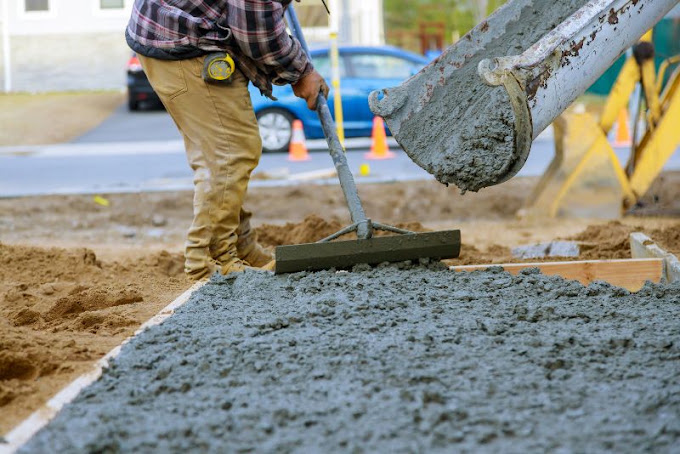 Worker raking and spreading a fresh concrete pour from a chute